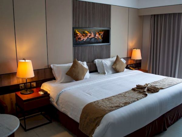 A cozy hotel room with a large bed, decorative pillows, warm lighting, and a modern wall design with a fireplace.