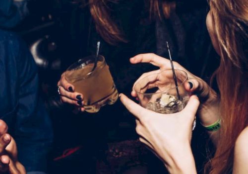 People are enjoying drinks at a social gathering. Laughter and conversation are evident, with cocktails in hand and a lively atmosphere.