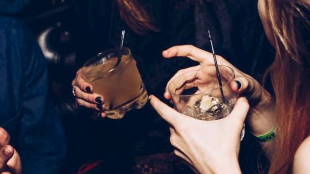 People are enjoying drinks at a social gathering. Laughter and conversation are evident, with cocktails in hand and a lively atmosphere.
