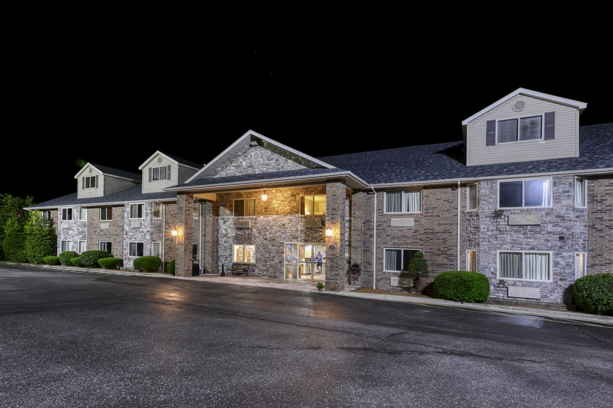 The image shows the exterior of a two-story brick building, possibly a hotel, at night with lights illuminating the façade.