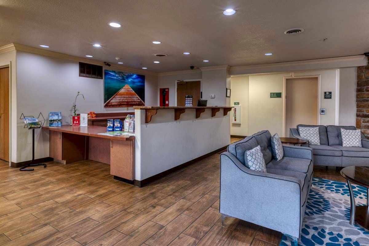 The image shows a hotel lobby with a reception desk, seating area, sofas, tables, and a landscape picture on the wall.