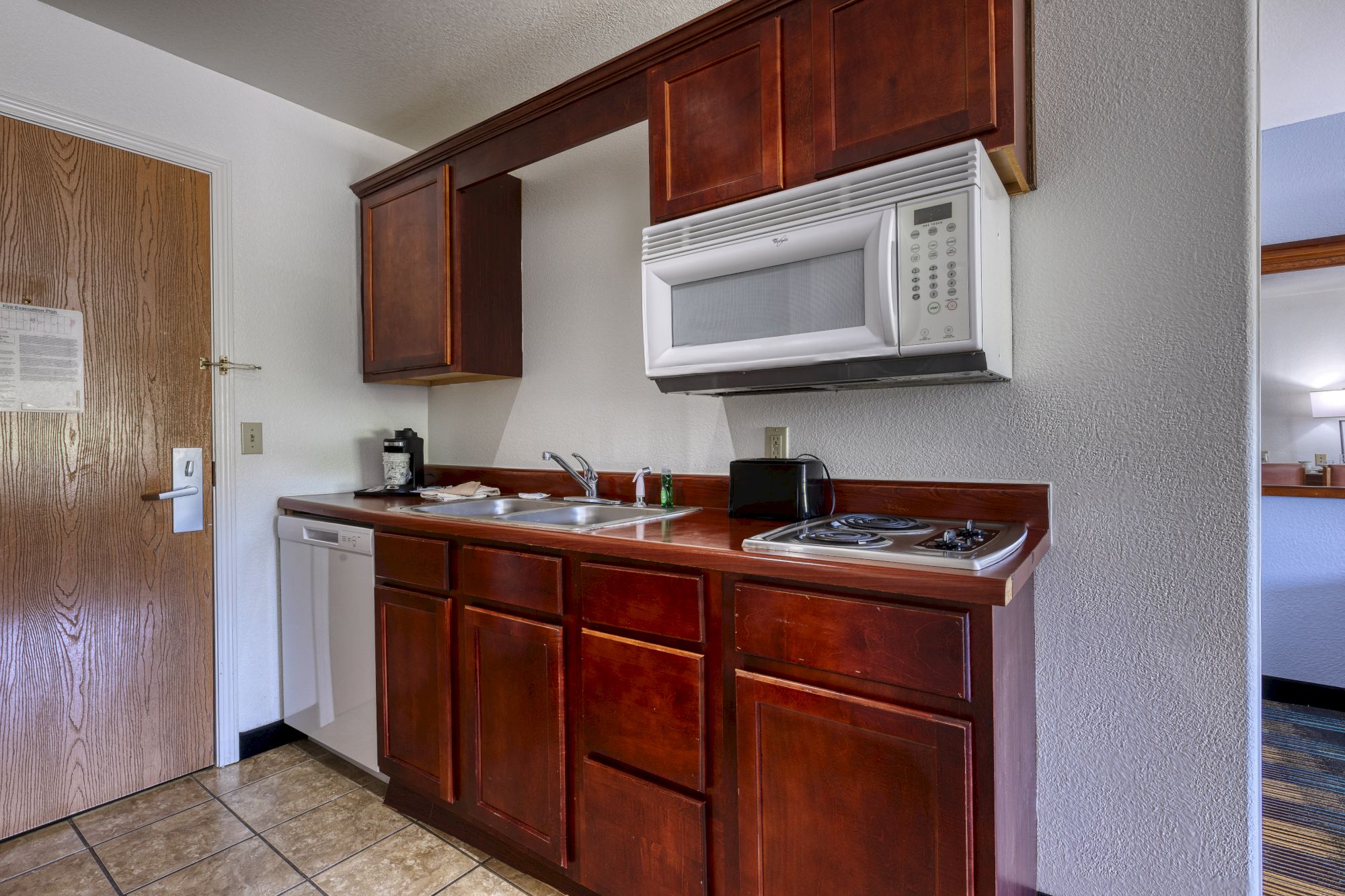 A small kitchenette with wooden cabinets, a sink, microwave, stovetop, and dishwasher in a compact space.