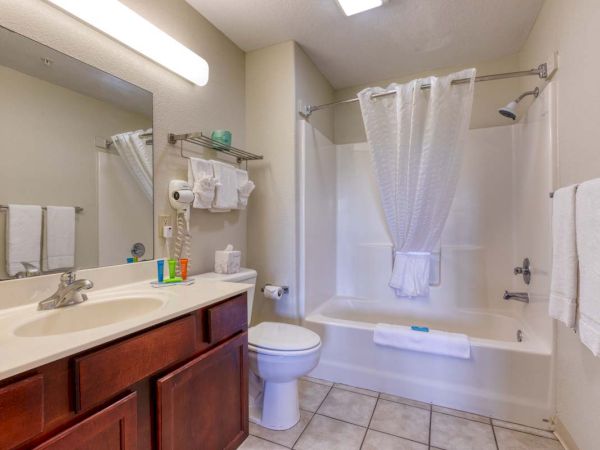 A clean bathroom with a sink, mirror, toiletries, towel rack, and a bathtub with a shower curtain.