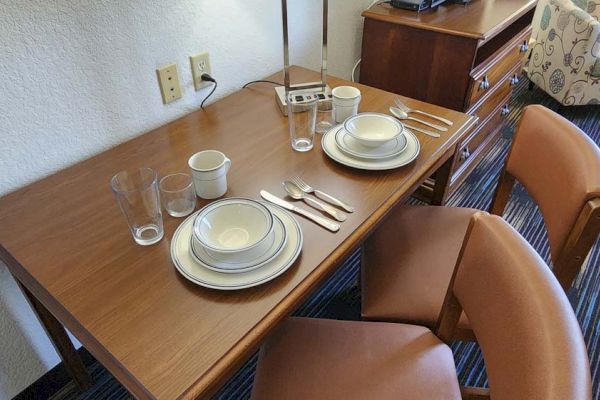 A table set for two with plates, bowls, glasses, cutlery, and cups. There's a lamp, and two chairs are placed beside the table.