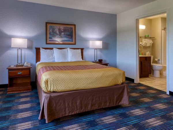 A hotel room with a bed, side tables, lamps, and a bathroom in the corner.
