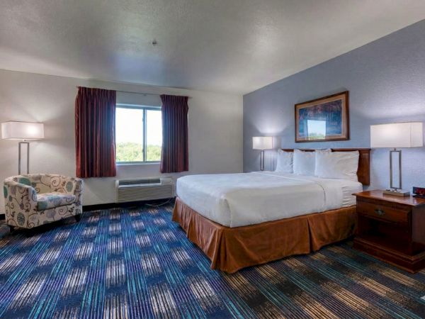 A standard hotel room with a large bed, two nightstands, lamps, a sitting chair, and a window with curtains.