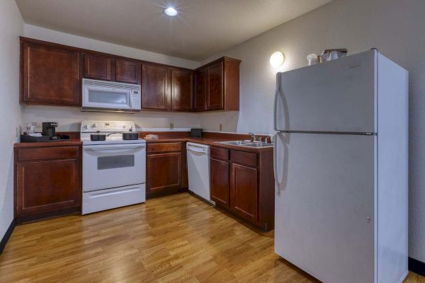 A kitchen with wooden cabinets, a stove, microwave, refrigerator, dishwasher, sink, and hardwood flooring.