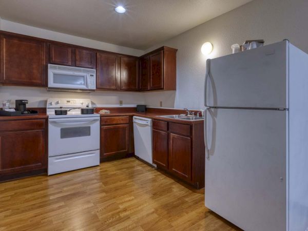 A kitchen with wooden cabinets, a stove, microwave, refrigerator, dishwasher, sink, and hardwood flooring.
