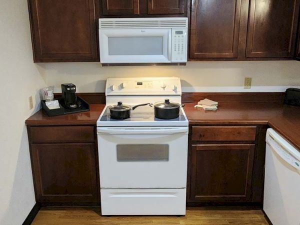 The image shows a kitchen with wooden cabinets, a stove with pots, a microwave, a coffee maker, and a dishwasher.