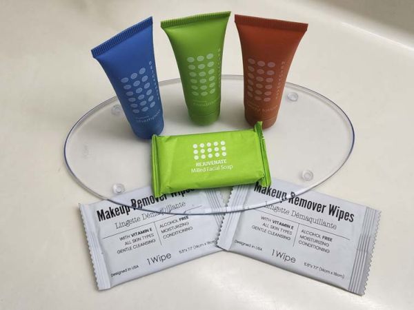 Hotel toiletries include shampoo, conditioner, lotion, soap, and makeup remover wipes on a countertop.