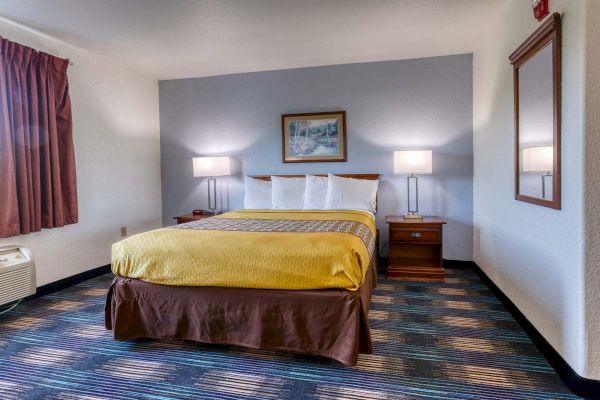 A hotel room with a double bed, two side tables with lamps, a wall mirror, framed artwork, and a striped carpet pattern.