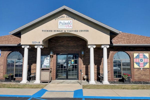 The image shows the entrance of the Pulaski County Tourism Bureau & Visitors Center, featuring columns and a sign above the door.