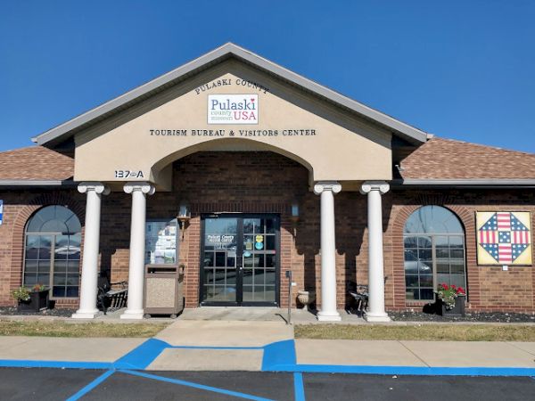 The image shows the entrance of the Pulaski County Tourism Bureau & Visitors Center, featuring columns and a sign above the door.