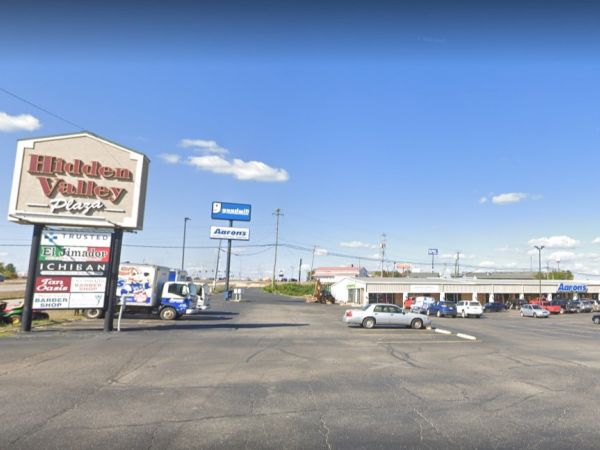 A parking lot with a sign labeled "Hickory Valley Plaza" and surrounding shops, vehicles are parked nearby.