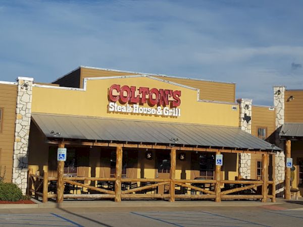 The image shows the exterior of Colton's Steak House & Grill with a wooden porch and accessible parking spots in front.