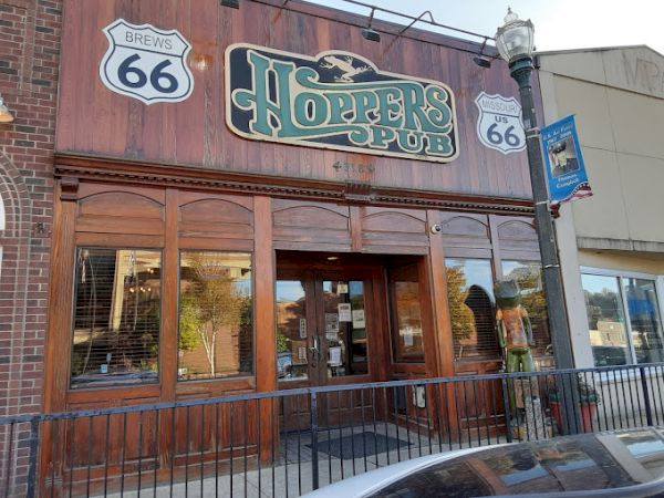 The image shows the exterior of Hopper's Pub on Route 66, featuring a wooden facade and signage, with a car parked in front.