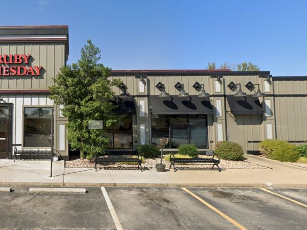 The image shows the exterior of a "Ruby Tuesday" restaurant with a parking lot in front and some plants and benches by the entrance.