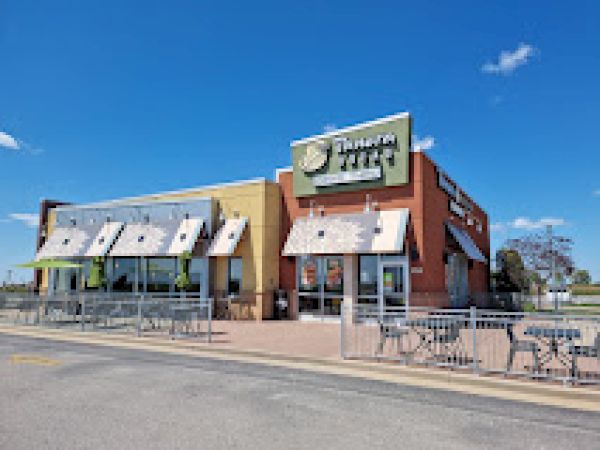 The image shows a Panera Bread restaurant with outdoor seating under a clear blue sky.