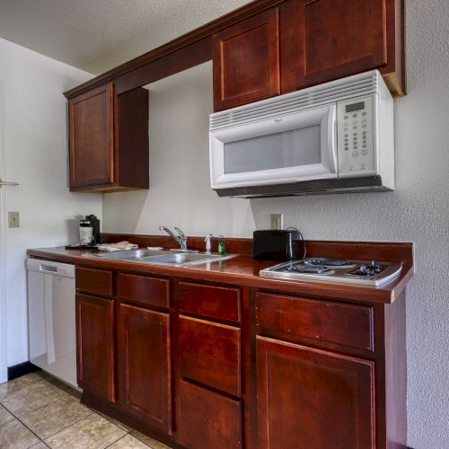 A compact kitchen area with wooden cabinets, a sink, microwave, stovetop, and a dishwasher in a small, cozy space.