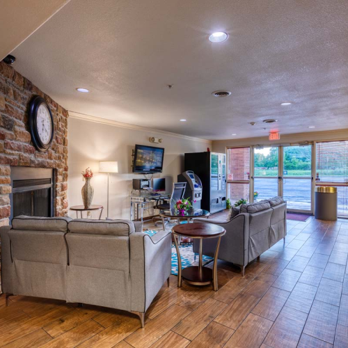 This image shows a cozy lounge area with sofas, a fireplace, a wall clock, a TV, and a vending machine, arranged on wooden flooring.