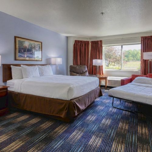 A cozy hotel bed setup with a wooden headboard, red curtains, patterned carpet, and a small desk by the window.
