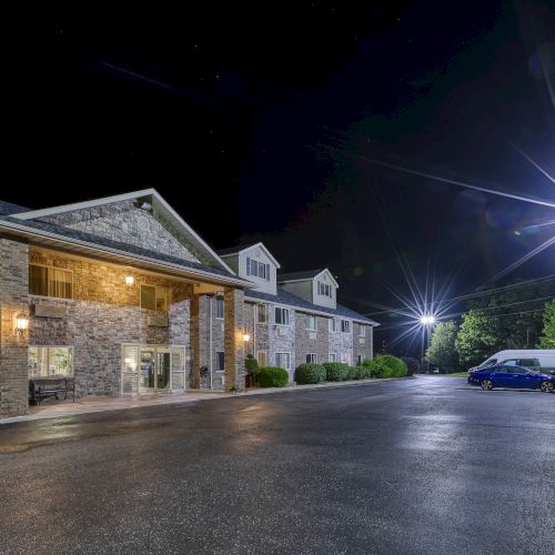 The image shows a well-lit building, likely a hotel, at night with two parked vehicles and streetlights illuminating the area.