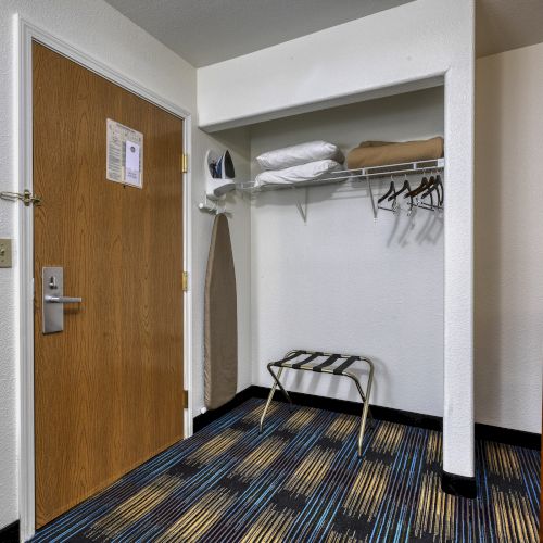 A hotel room entryway with a closet area. There's an ironing board, iron, hangers, folded linens, a luggage rack, and a painting on the wall.