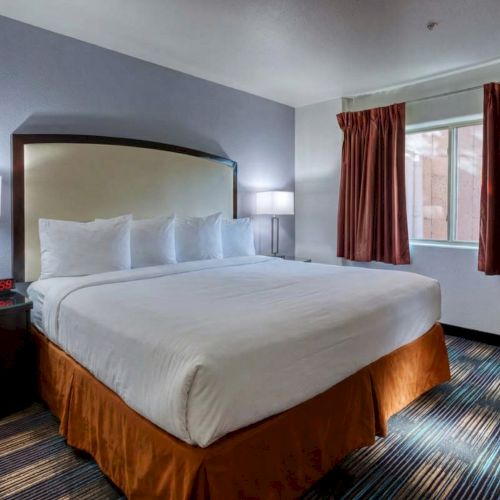 A well-made hotel room with a large bed, bedside tables, a desk, a chair, a flat-screen TV, and warm lighting.