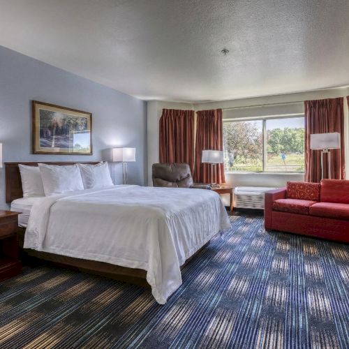 A classic hotel room with two twin beds, a desk, and a red-carpeted floor; windows with red drapes and soft lighting.