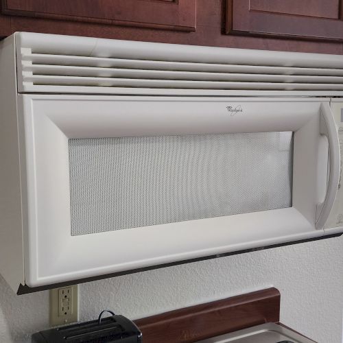 This image shows a microwave mounted above a kitchen counter, with a glimpse of a room in the background.
