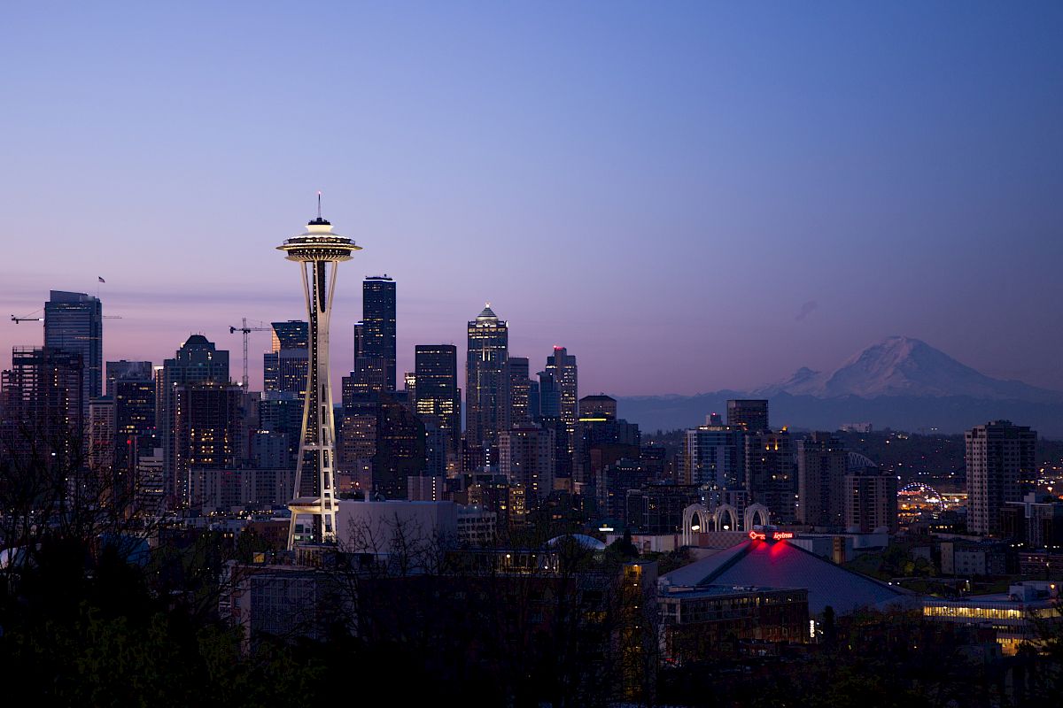 Seattle skyline at dusk with the Space Needle prominently visible and Mount Rainier in the background under a clear sky.
