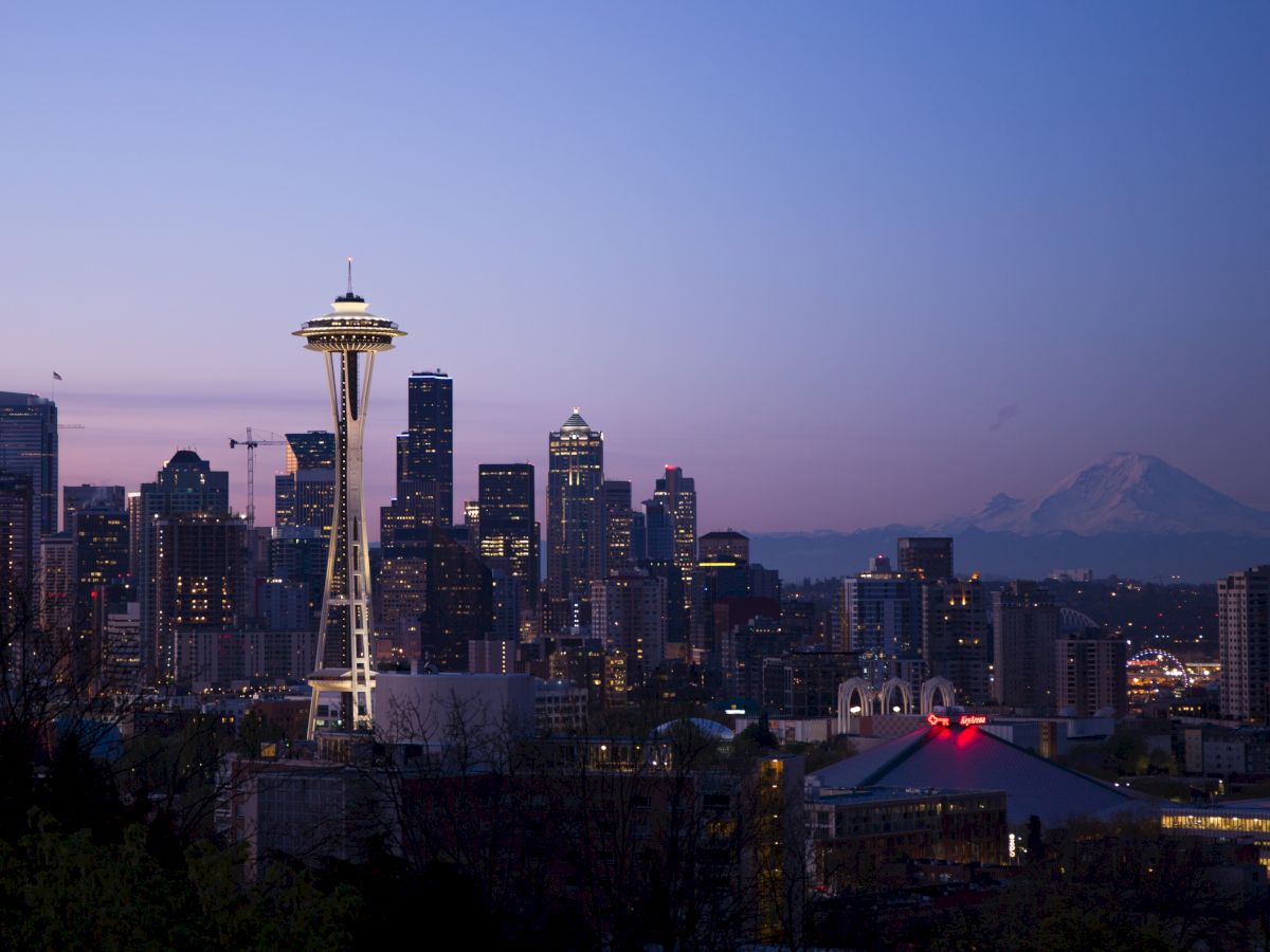 Seattle skyline at dusk with the Space Needle prominently visible and Mount Rainier in the background under a clear sky.